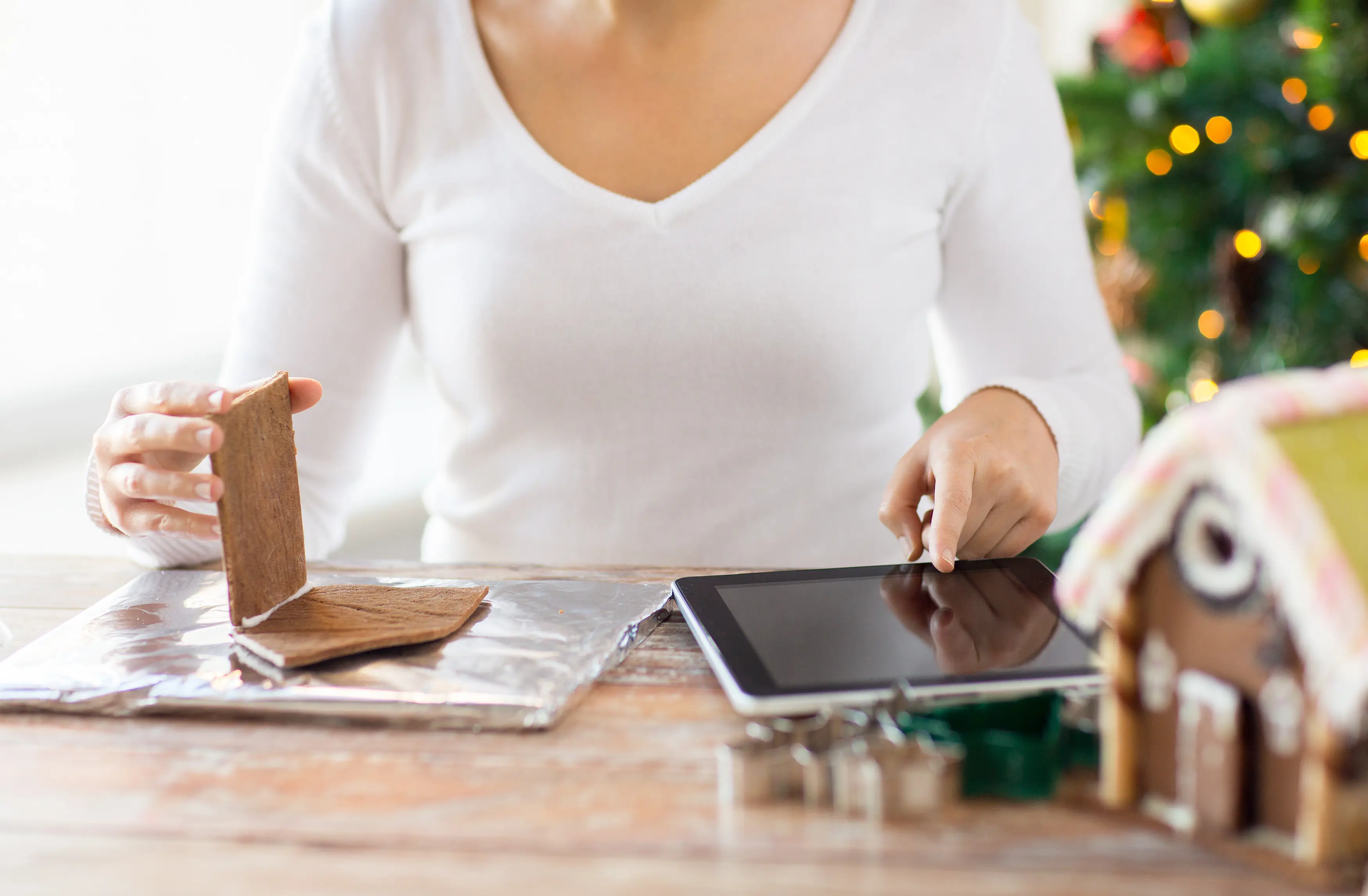 Konzept zu Kochen, Menschen, Weihnachten und Technologie – Nahaufnahme einer Frau, die zu Hause mit einem Tablet-Computer Lebkuchenhäuser macht.